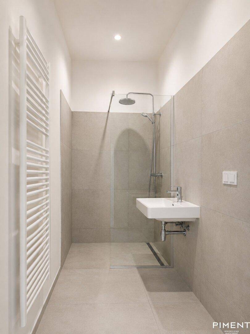 Modernes Badezimmer mit ebenerdiger Dusche, Wandheizkörper und hellen Fliesen.