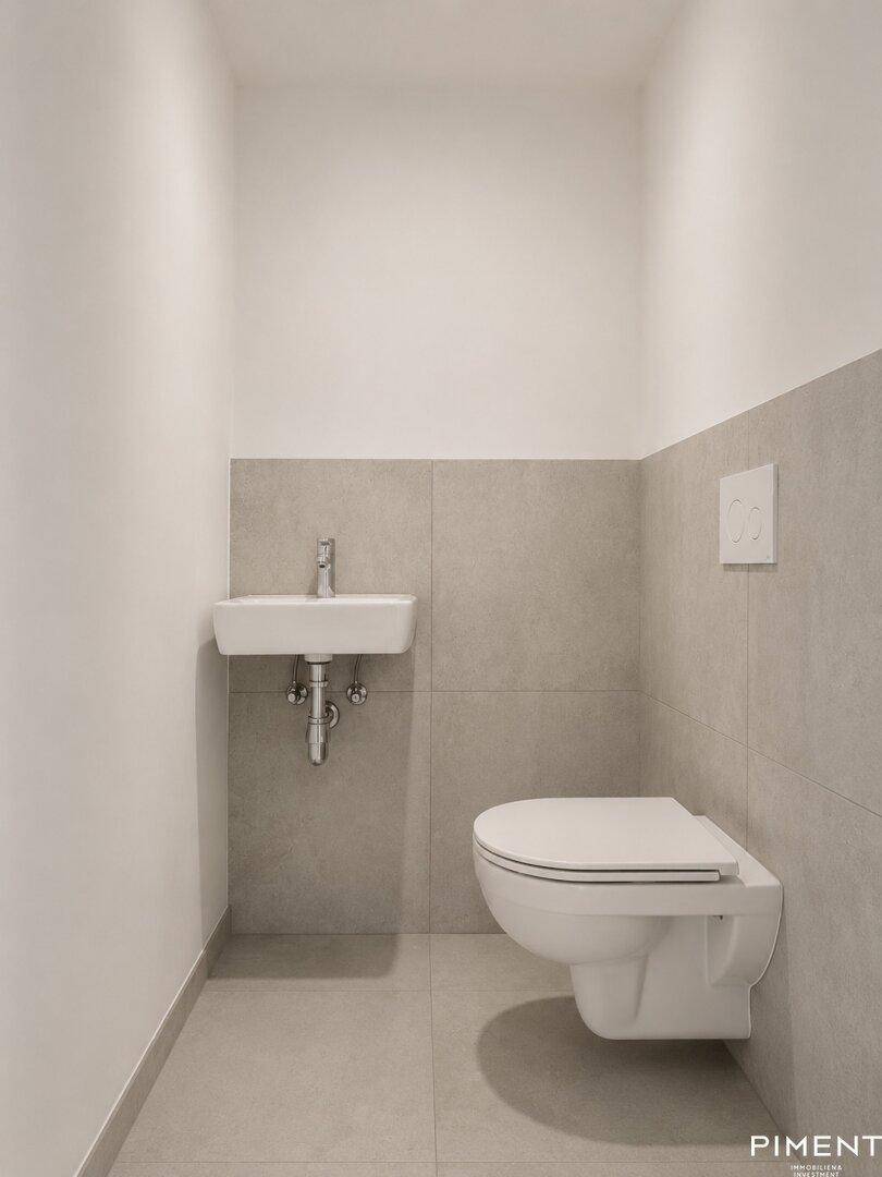 Separates Gäste-WC mit Wand-WC, kleinem Waschbecken und modernen Fliesen.