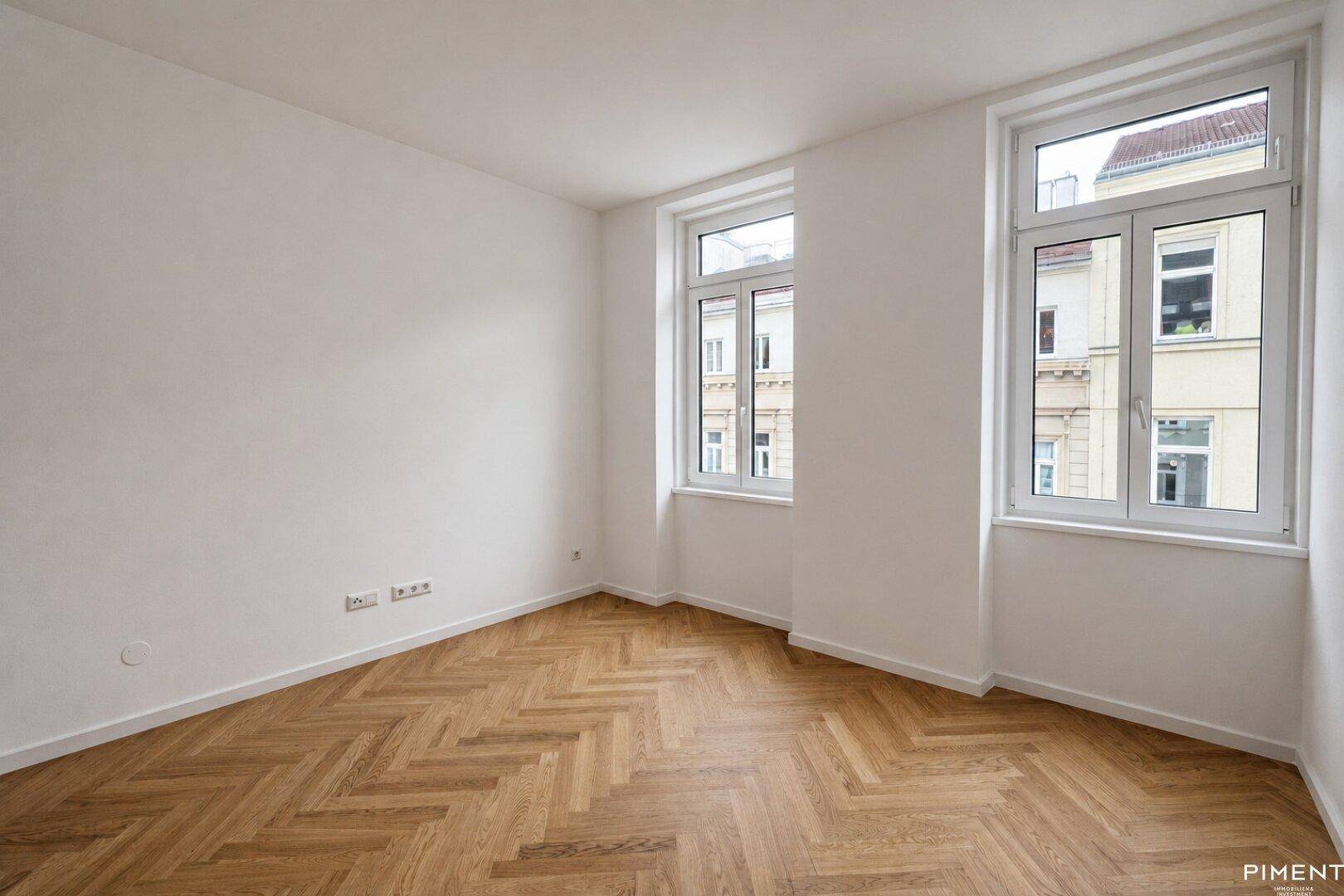 Ruhiges Zimmer mit Fischgrätparkett und zwei großen Fenstern mit Stadtblick.