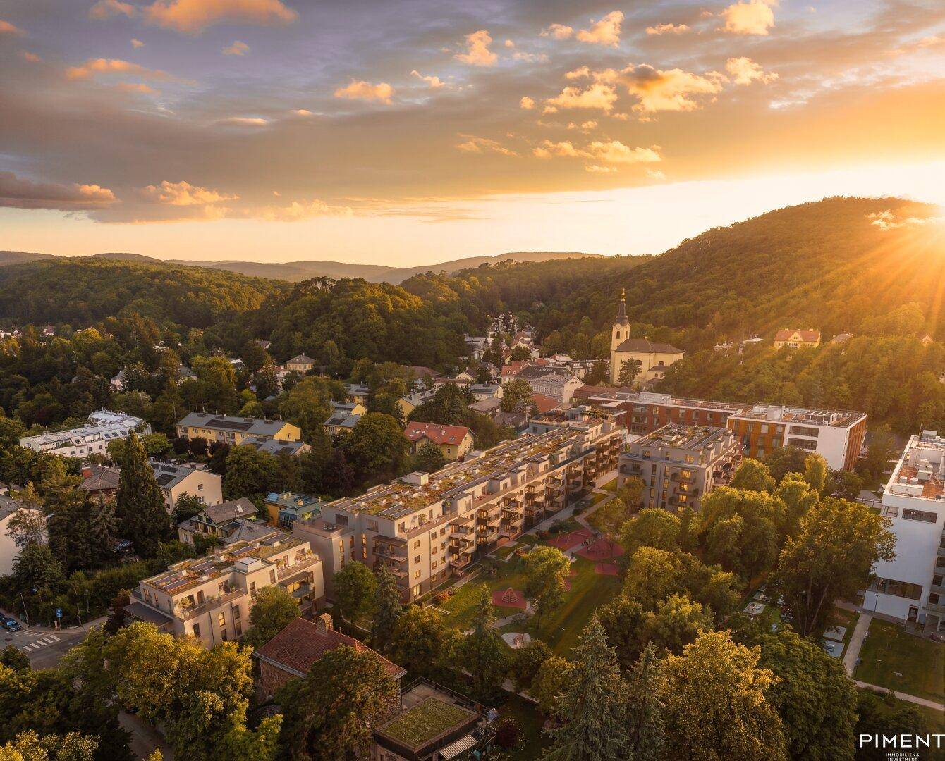 Luftaufnahme eines modernen Wohnkomplexes in hügeliger Landschaft bei Sonnenuntergang.