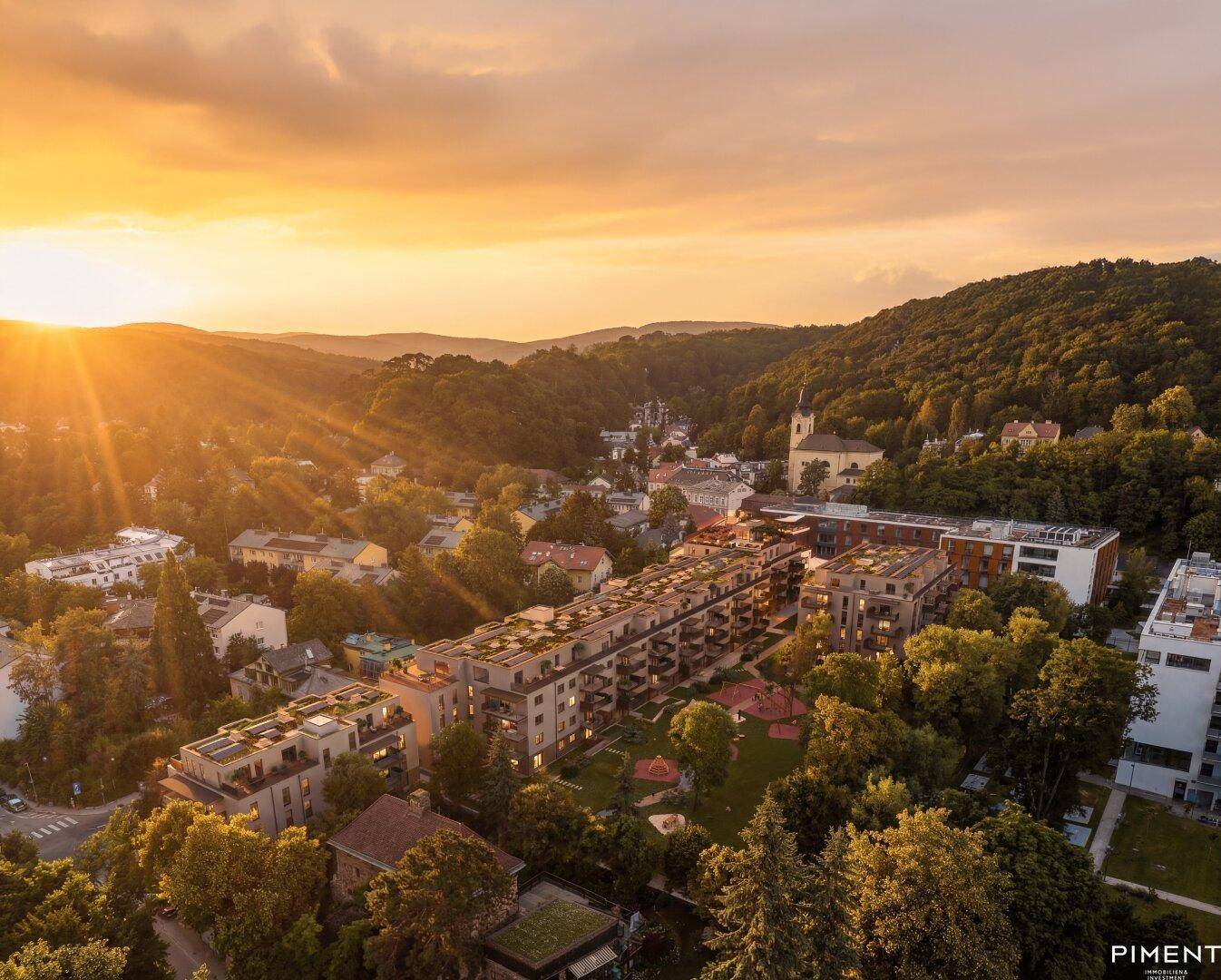 Abendliche Luftaufnahme des Wohnkomplexes, eingebettet in die grüne Hügellandschaft bei Sonnenuntergang.