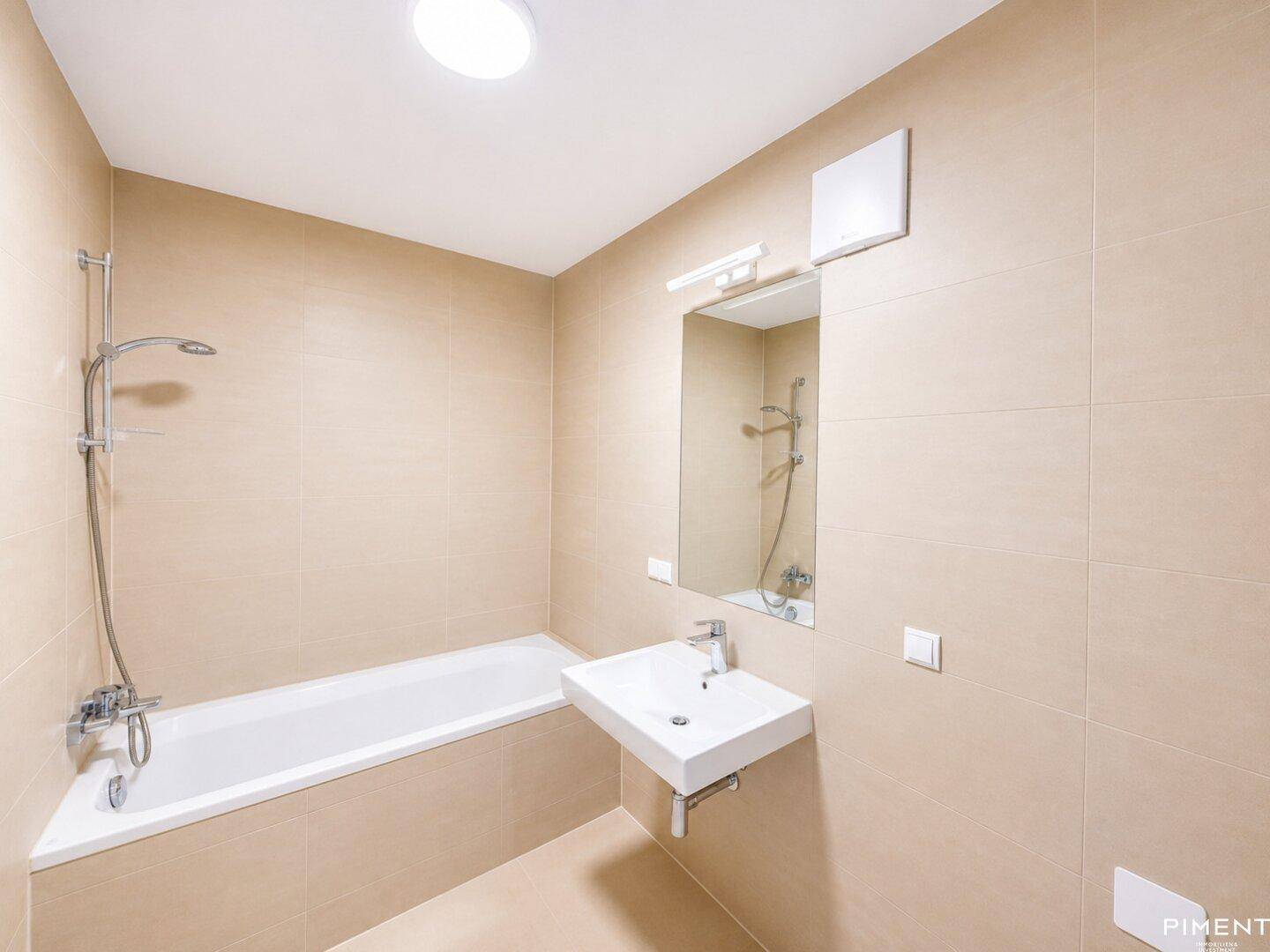 Modernes Badezimmer mit beigefarbenen Fliesen, Badewanne mit Duschfunktion und Einzelwaschbecken.