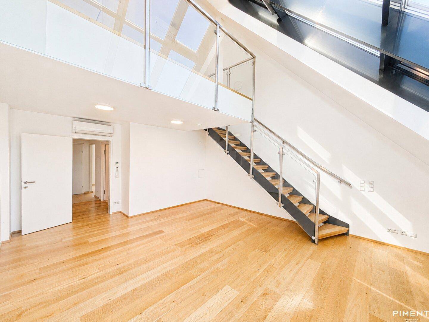 Helles, offenes Wohnzimmer mit Holzfußboden, moderner Treppe und großen Dachfenstern für viel Tageslicht.