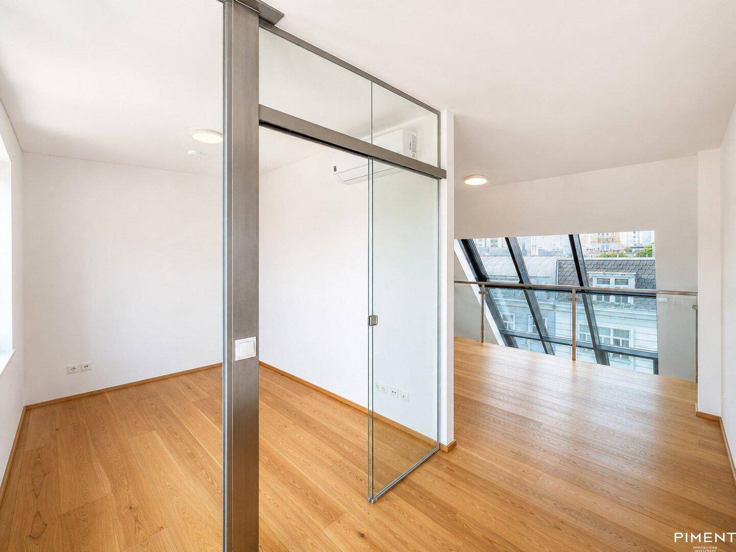 Heller Wohnbereich mit Glasschiebetür, Holzfußboden und Blick auf die Stadt durch große Fenster.