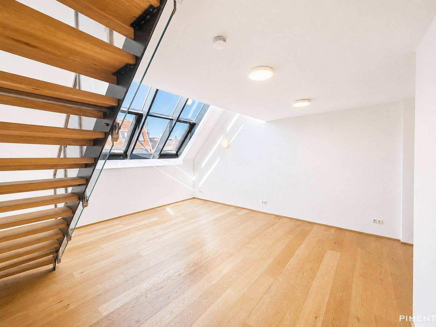 Leerer Raum mit Holztreppe, Dachfenstern und hellem Parkettboden.