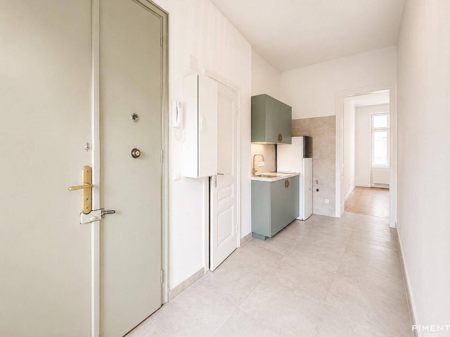 Eingangsbereich mit kompakter Küchenzeile und grauen Fliesen, direkt neben der grünen Wohnungstür.