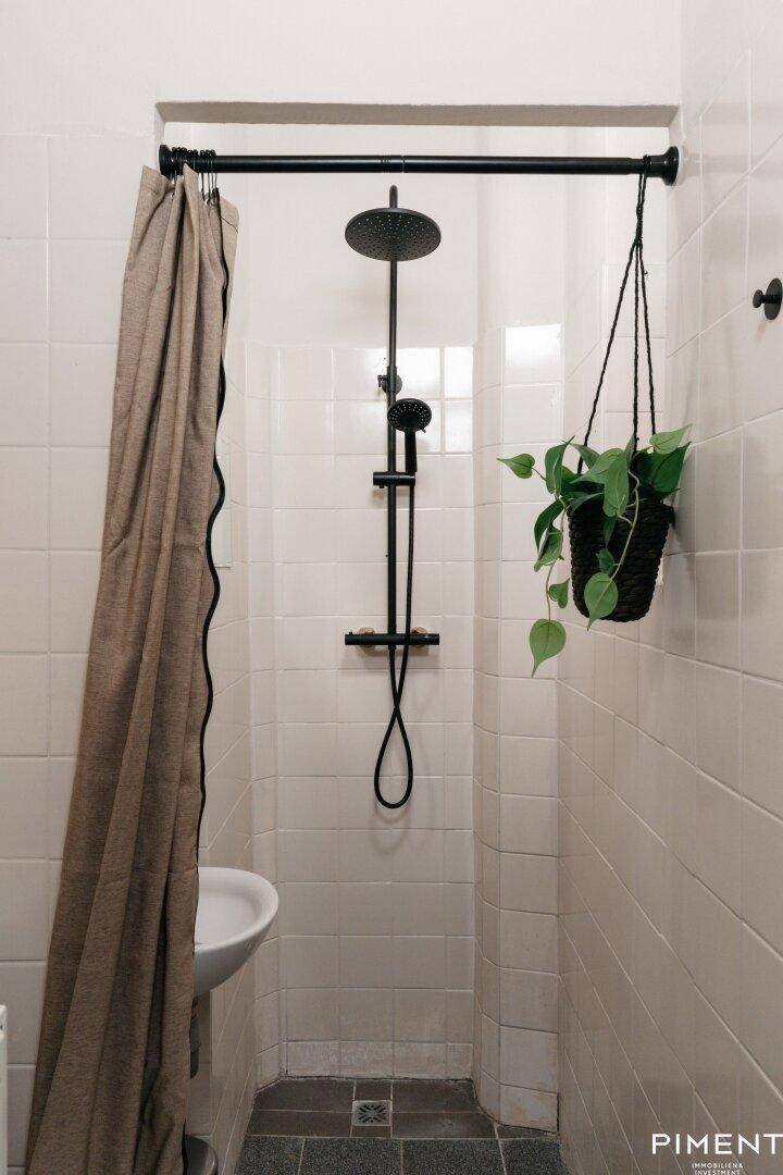 Modern geflieste Dusche mit schwarzer Regendusche und hängender Pflanze.