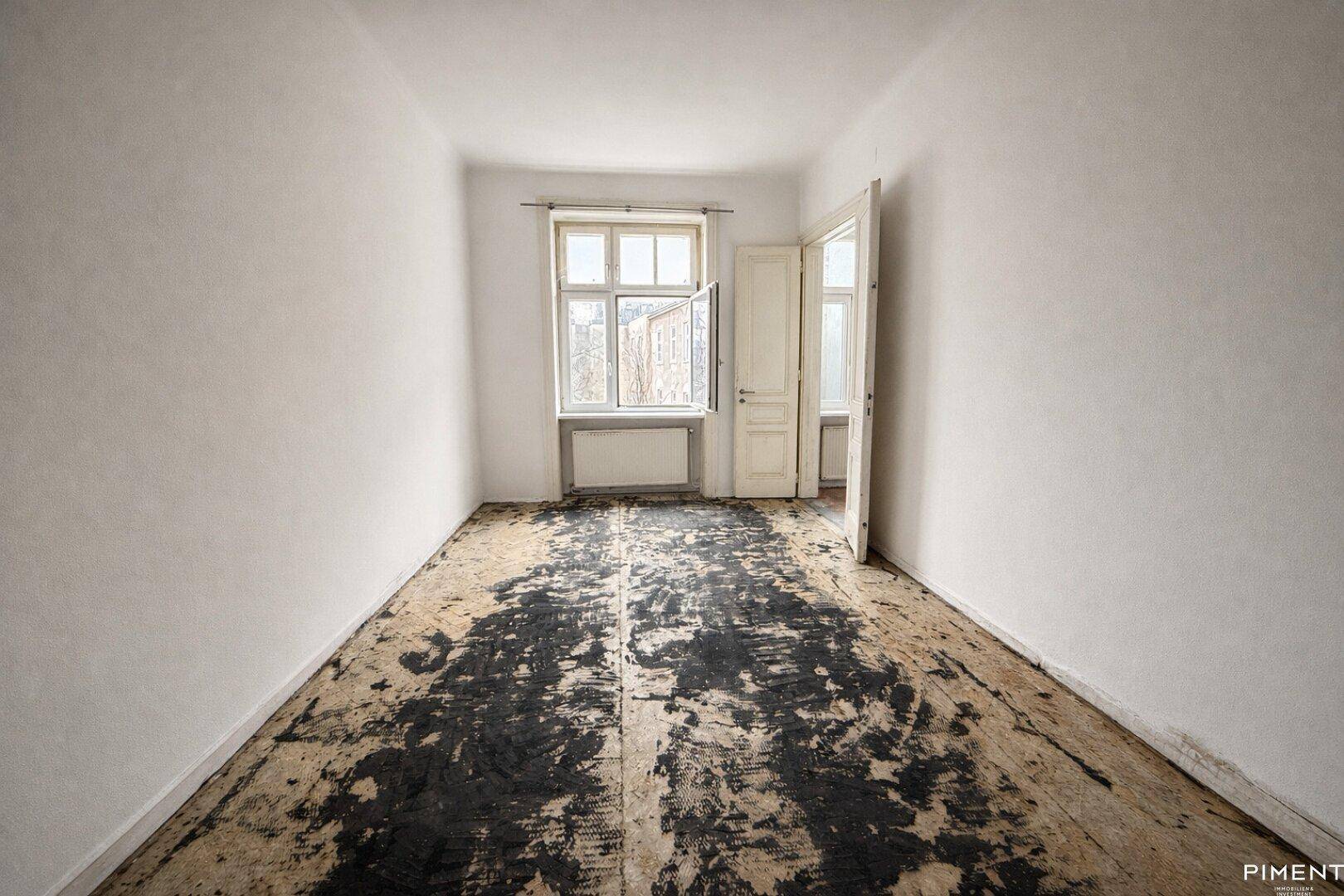 Leerer Raum mit freigelegten Dielen und einem Fenster, bereit für die Renovierung.
