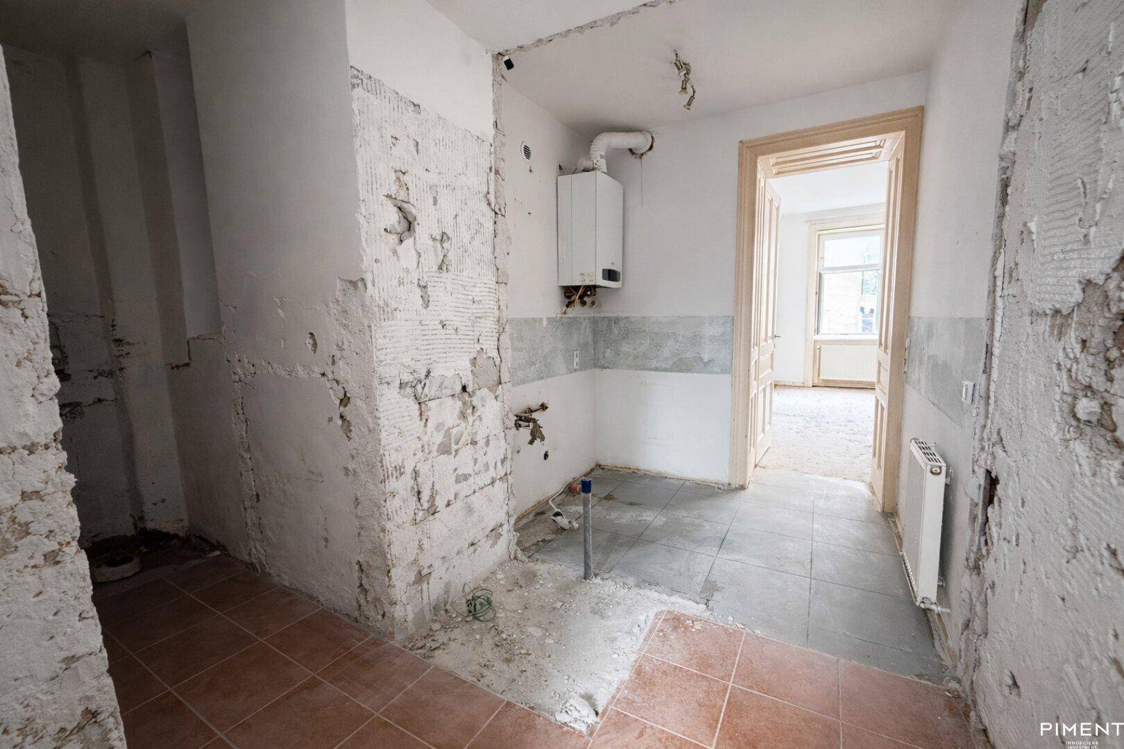 Küche im Rohbau mit freigelegten Wänden, Heizkessel und Fliesenboden.