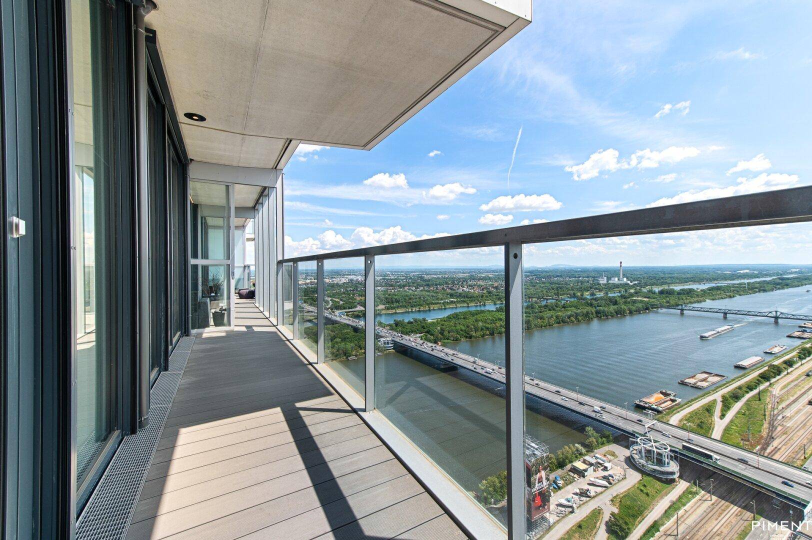 Langer Balkon mit Glasgeländer und weitem Blick über den Fluss und die Stadtlandschaft.