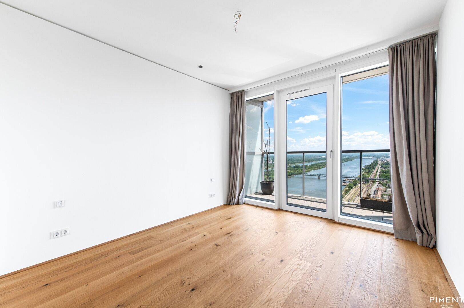 Helles Zimmer mit Holzboden, weißen Wänden und Zugang zu einem Balkon mit Flussblick.