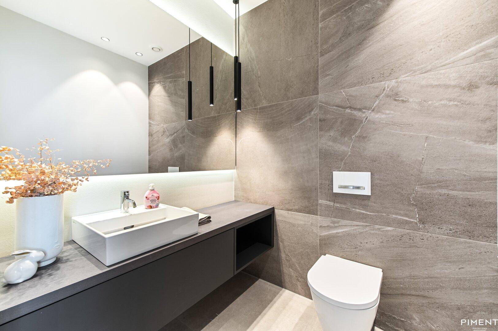 Modernes Gäste-WC mit eleganten grauen Fliesen und einem stilvollen Waschbecken.