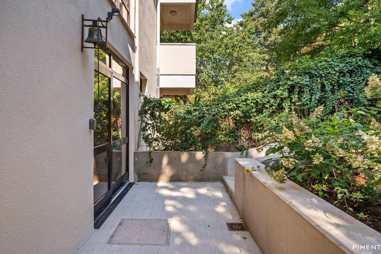 Kleiner, gepflasterter Terrassenbereich mit Zugang zum Gebäude und viel Grün.