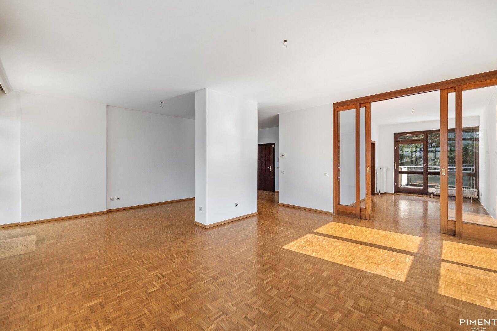 Offener Wohnbereich mit Parkettboden und Schiebetüren zu einem weiteren Zimmer.