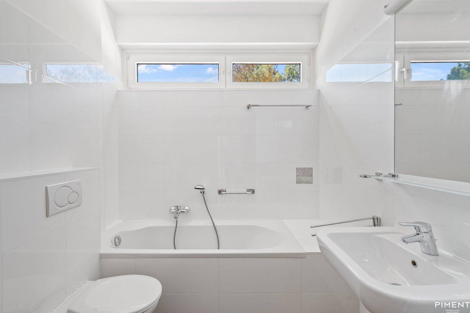 Modernes Badezimmer mit weißen Fliesen, Badewanne und Fenster für Tageslicht.