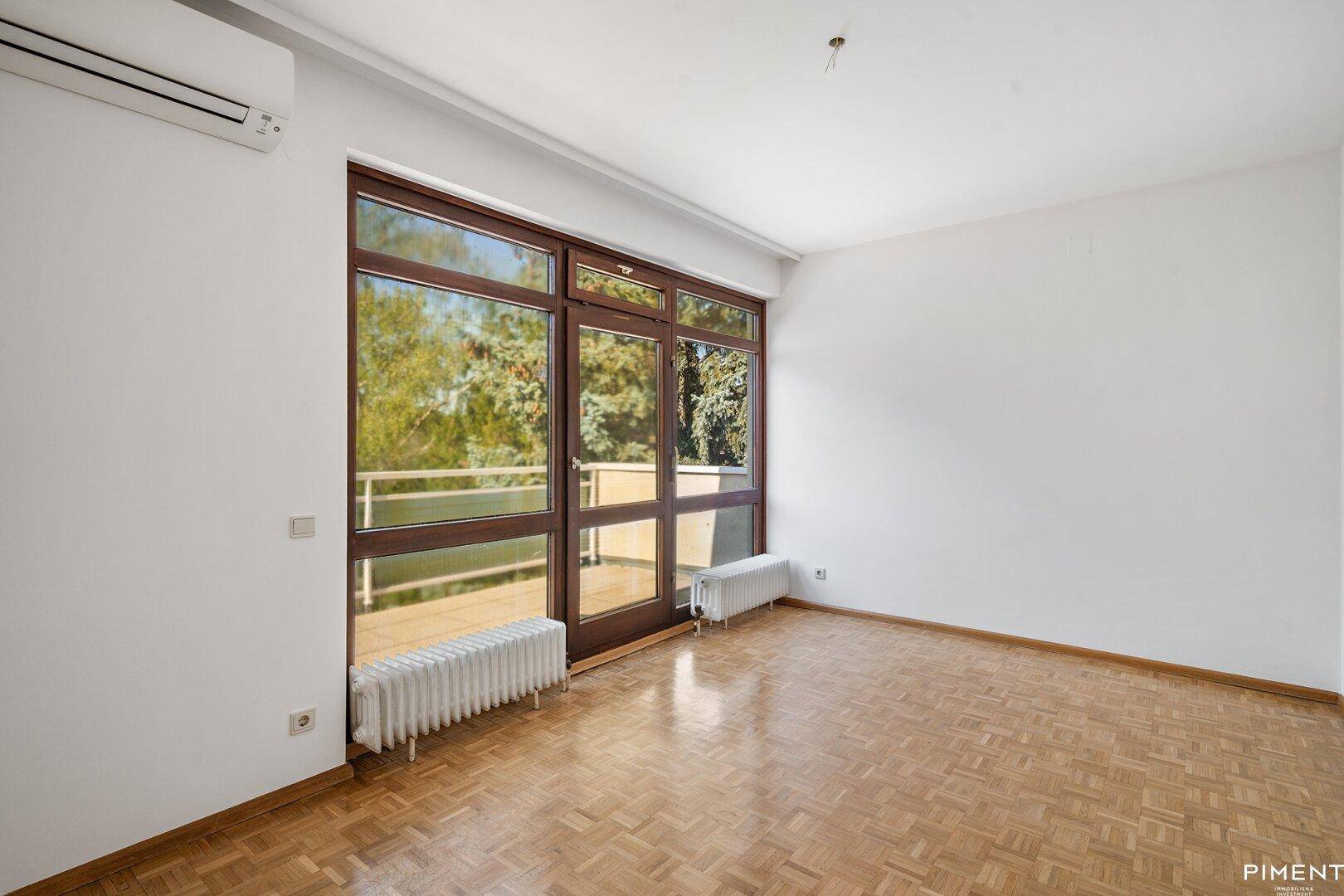 Helles Schlafzimmer mit Parkettboden, Klimaanlage und Zugang zu einem Balkon oder Terrasse.