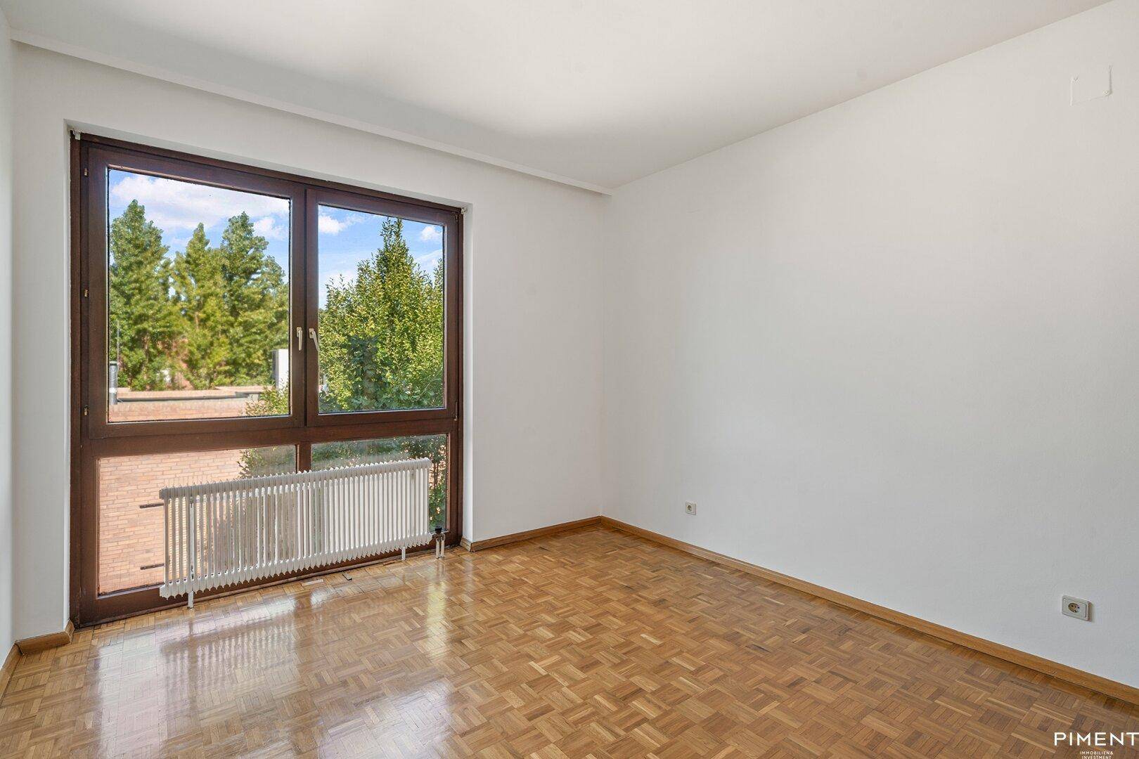 Geräumiges Schlafzimmer mit Parkettboden und großem Fenster mit Blick ins Grüne.