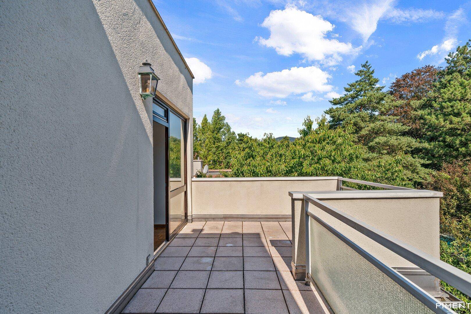 Sonniger Terrassenbereich mit Fliesenboden und Blick auf die umliegende Natur und Bäume.