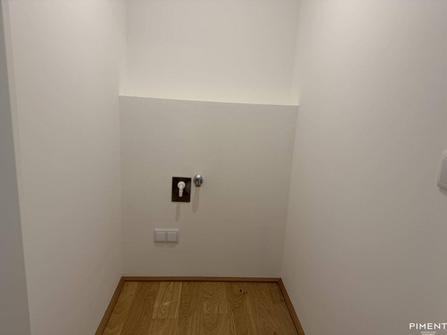 Praktischer Hauswirtschaftsraum mit Holzboden und Anschlüssen für Waschmaschine, bietet zusätzlichen Stauraum.