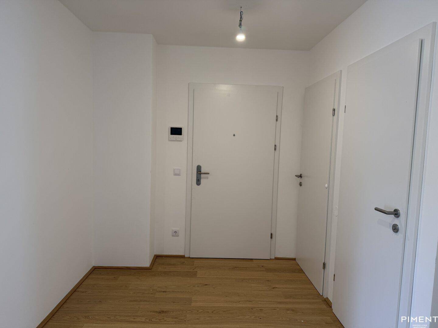 Heller Eingangsbereich mit Holzboden und mehreren Türen, ausgestattet mit einer Gegensprechanlage.
