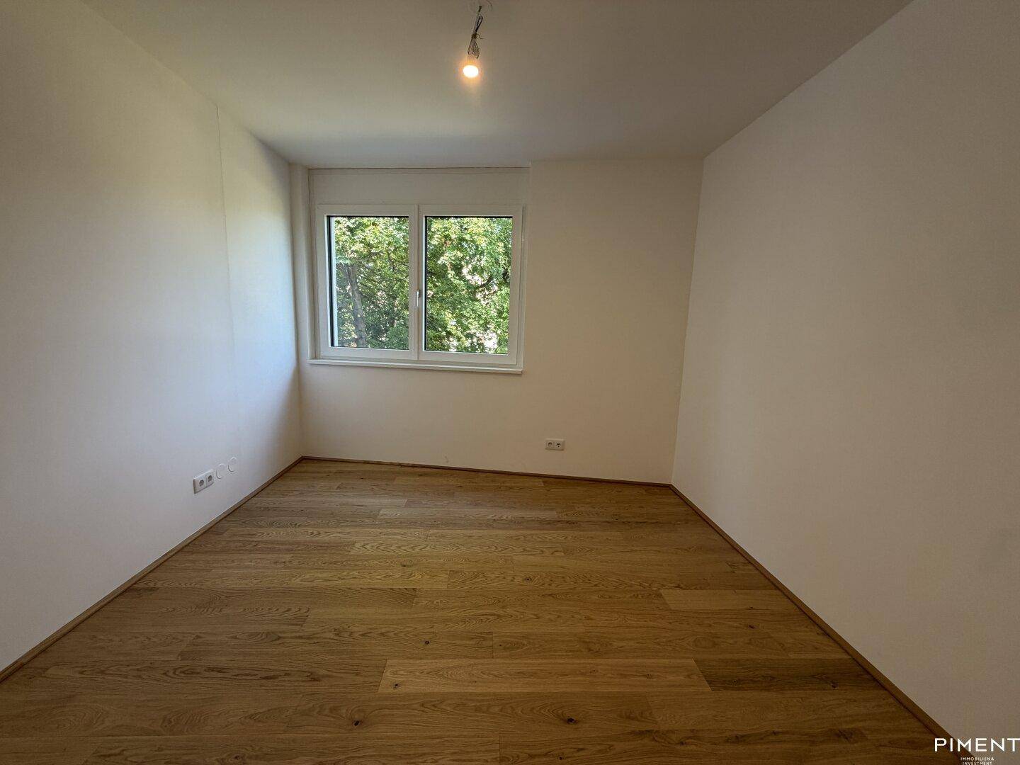 Ruhiges Zimmer mit Holzboden und Fensterblick ins Grüne, ideal als Schlaf- oder Arbeitszimmer.