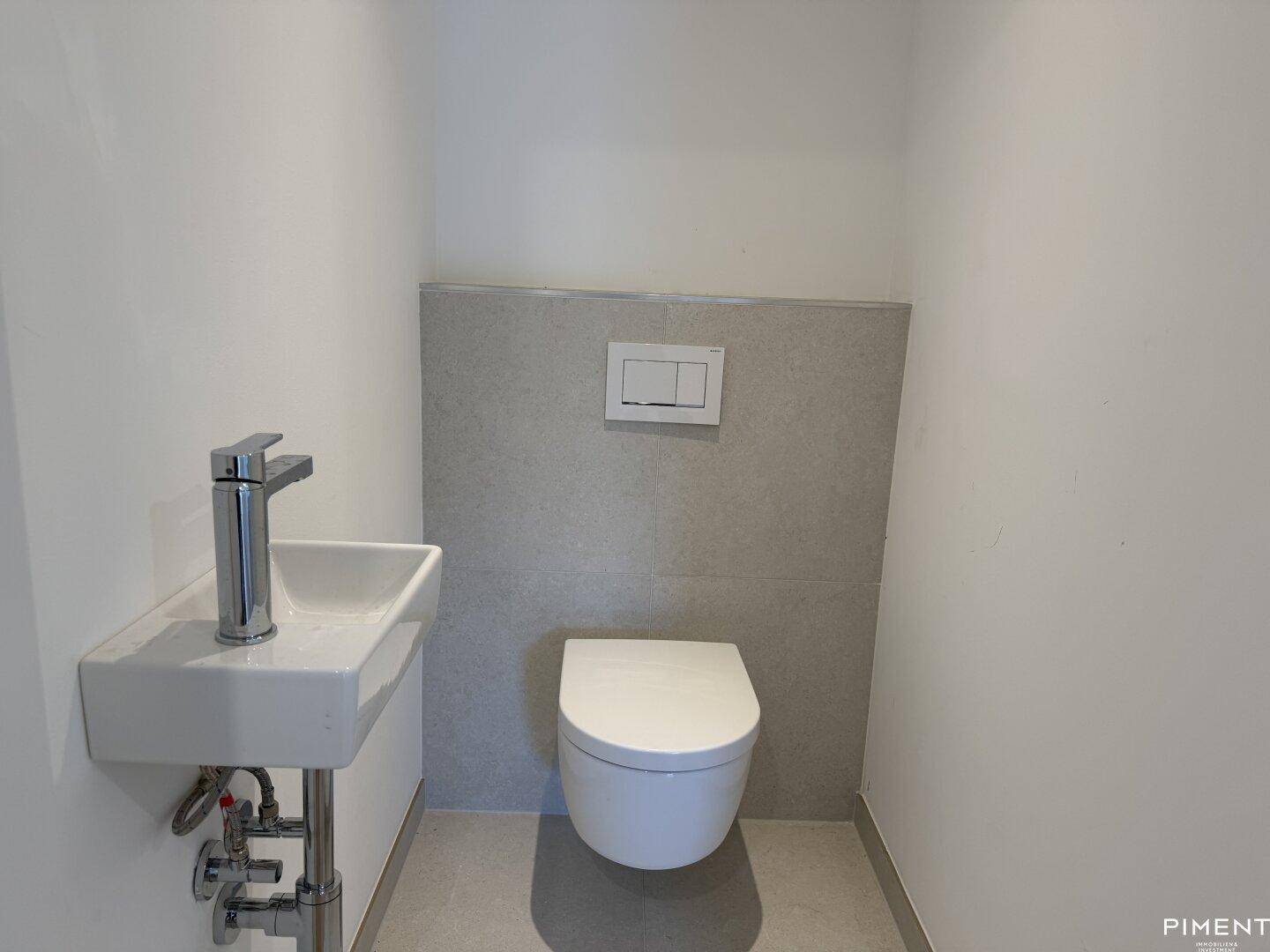 Modernes Gäste-WC mit wandhängender Toilette und kleinem Waschbecken, in hellen Farbtönen gehalten.