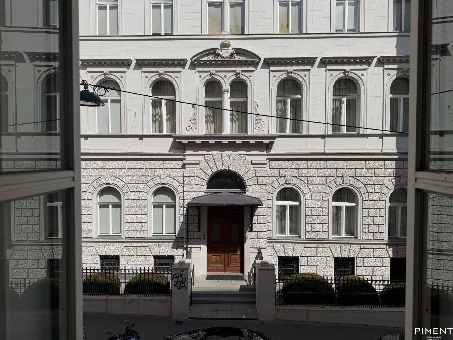 Blick aus dem Fenster auf die detailreiche Fassade eines gegenüberliegenden Gebäudes mit klassischen Elementen.