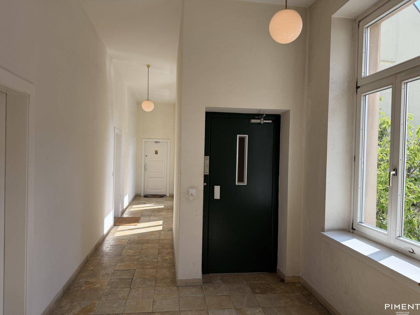 Heller Eingangsbereich des Gebäudes mit Fliesenboden, großen Fenstern und Zugang zum Aufzug.