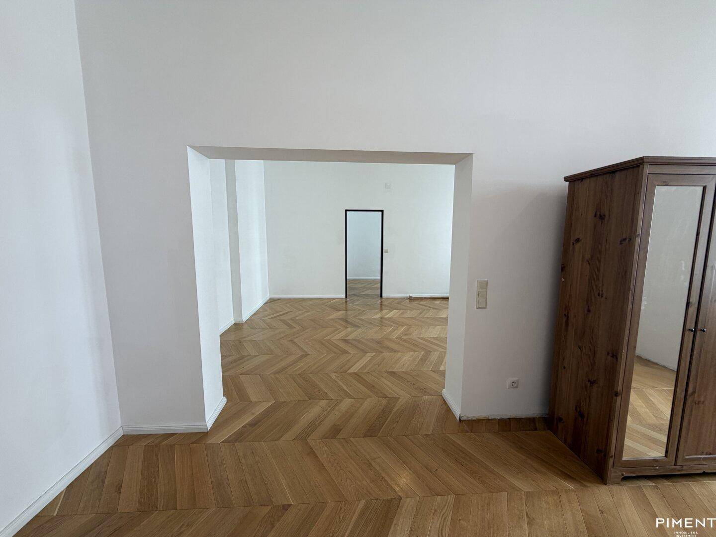 Offener Durchgang zu einem weiteren geräumigen Zimmer mit elegantem Fischgrätparkettboden.