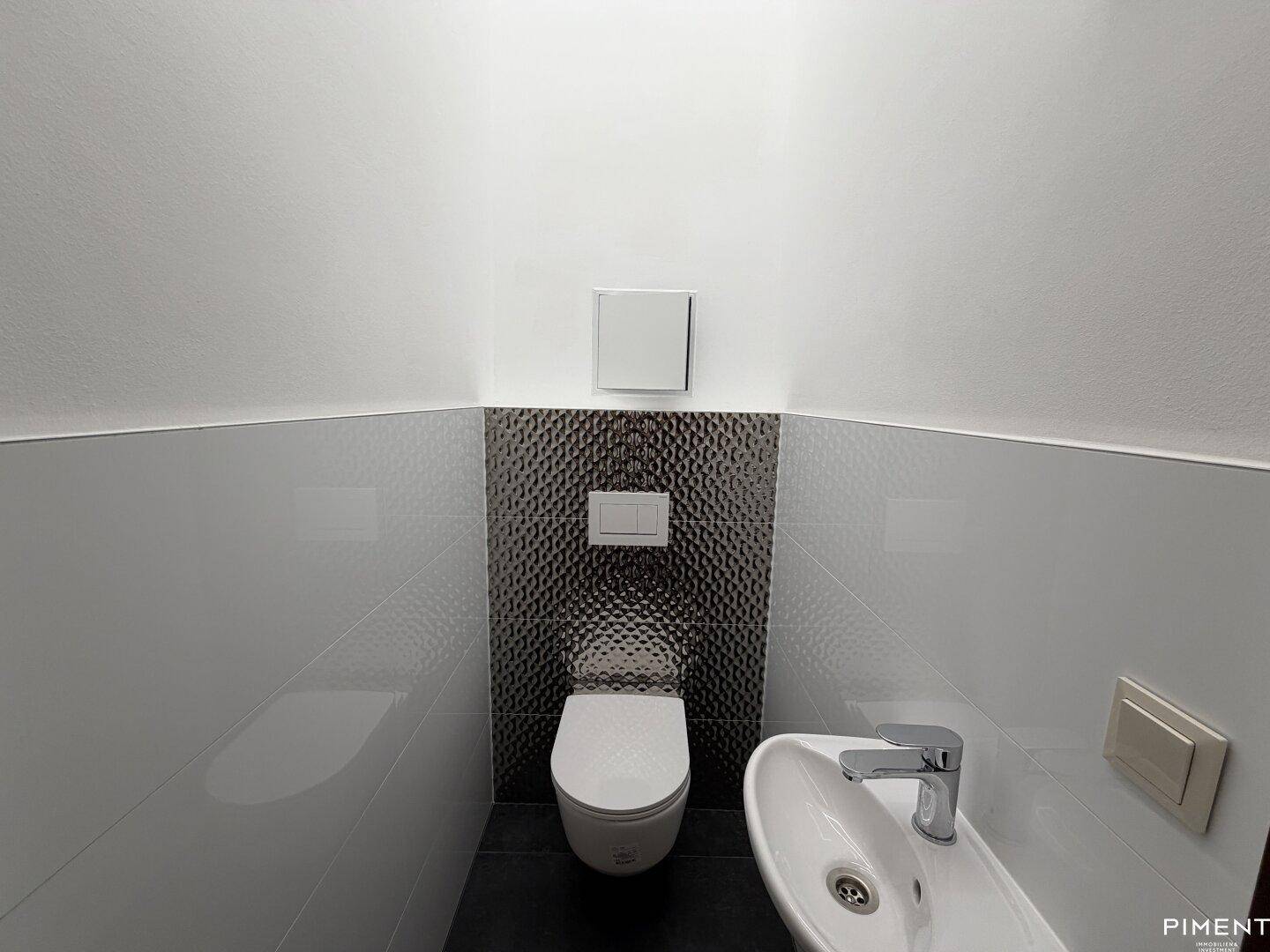 Modernes Gäste-WC mit wandhängender Toilette, kleinem Waschbecken und stilvollen dunklen Fliesen.