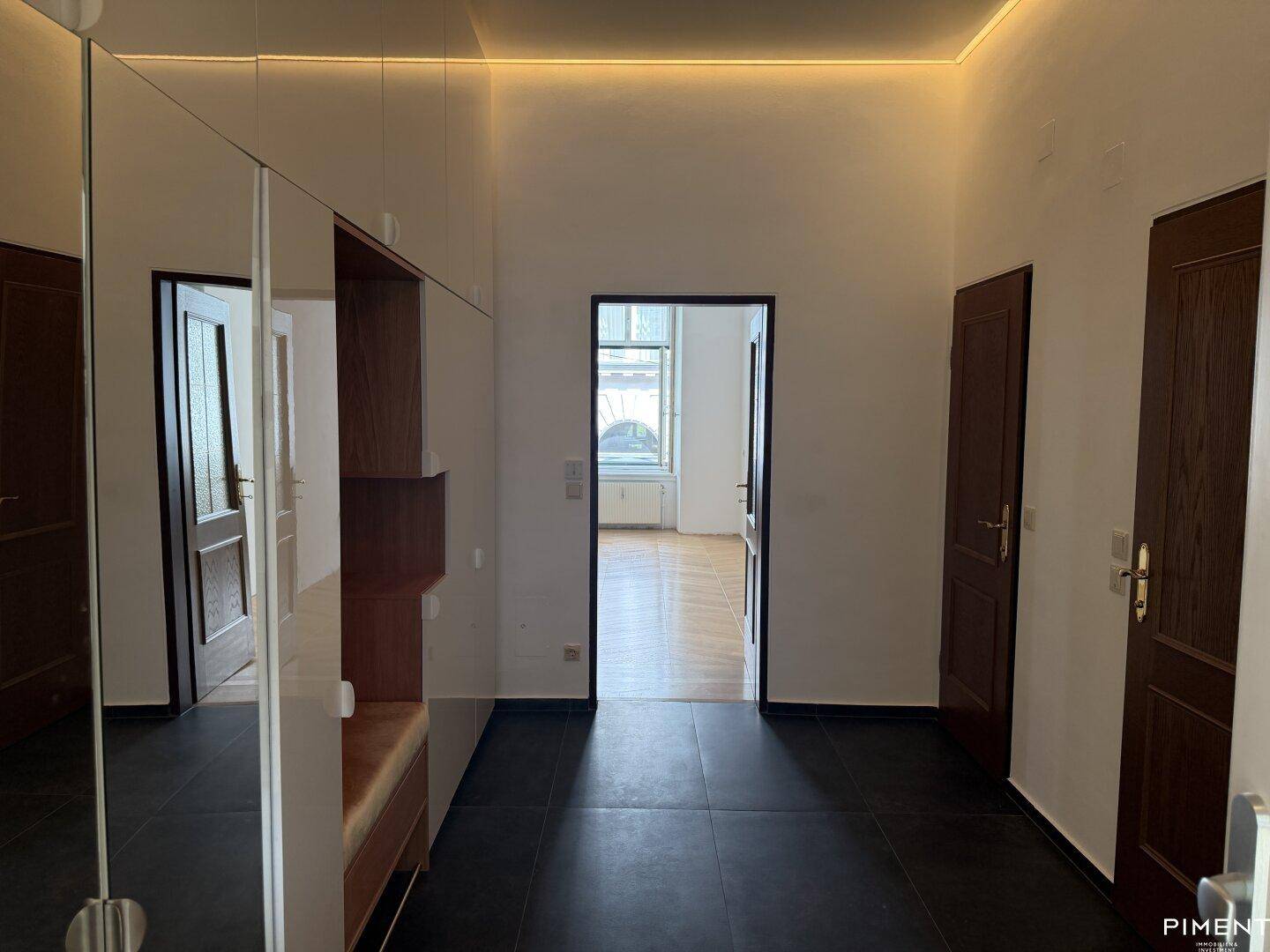 Heller Flur mit dunklen Fliesen, Spiegelfronten und Zugang zu weiteren Räumen der Wohnung.