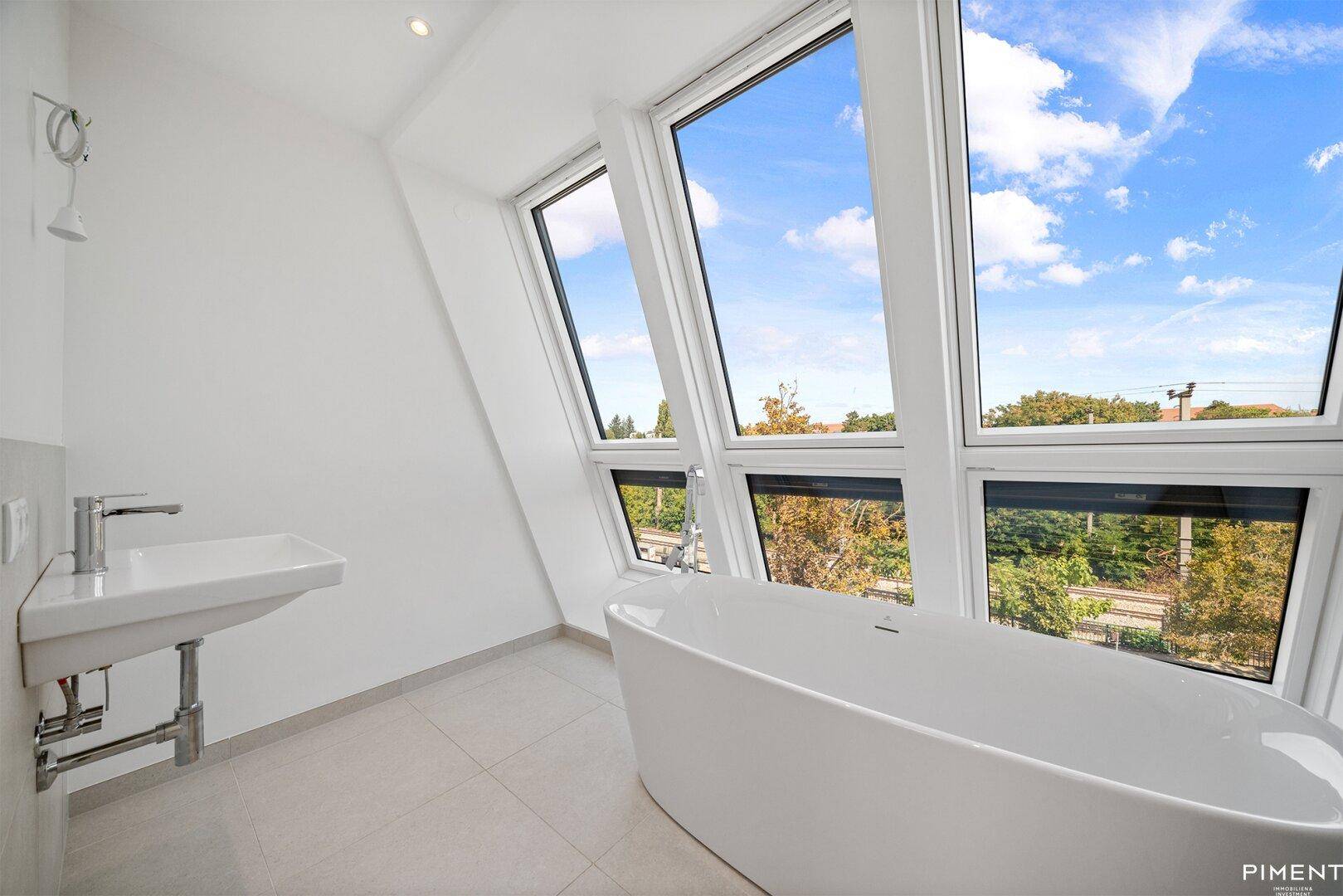 Modernes Badezimmer im Dachgeschoss mit freistehender Badewanne und großen Fenstern.