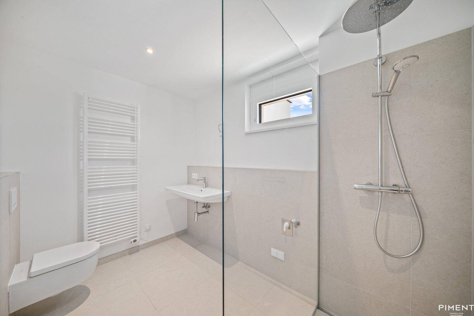 Helles Badezimmer mit ebenerdiger Dusche, wandhängendem WC und beheiztem Handtuchhalter.