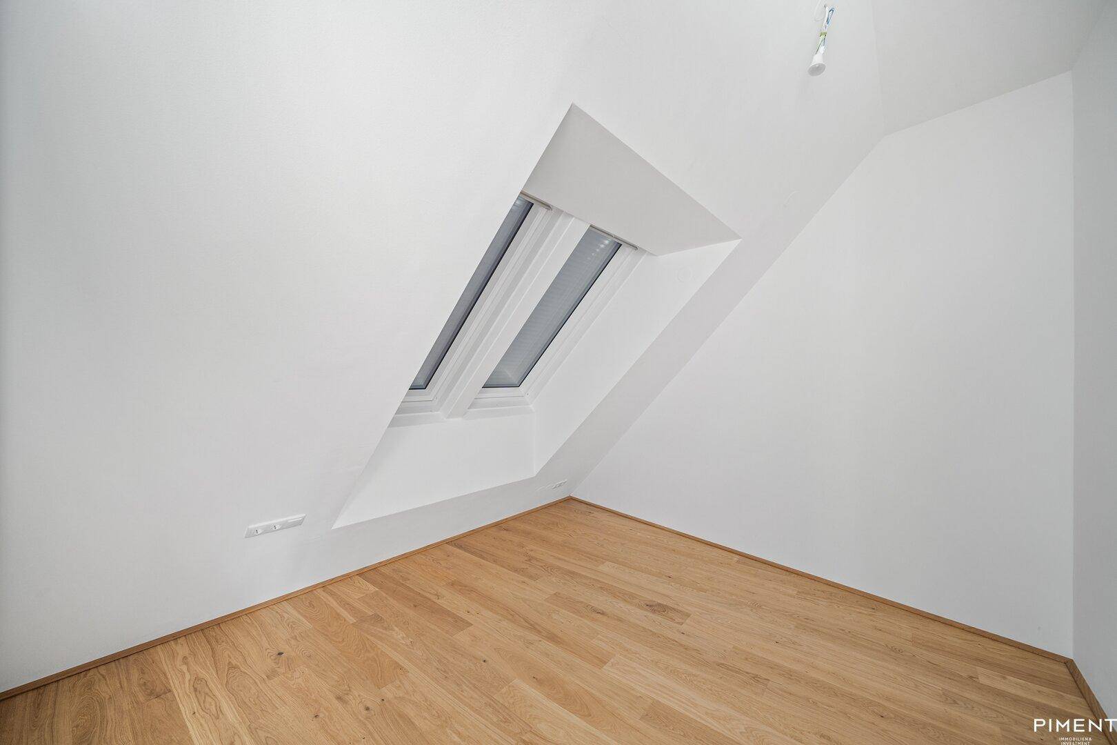 Ruhiges Dachgeschosszimmer mit Holzboden und einem großen Dachfenster für viel Tageslicht.