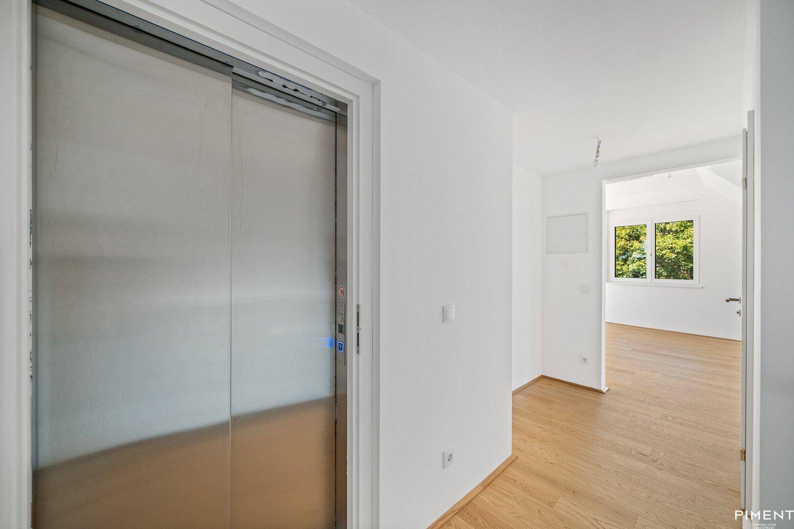 Heller Flur mit Holzboden und modernem Aufzug, der zu den Wohnbereichen führt.