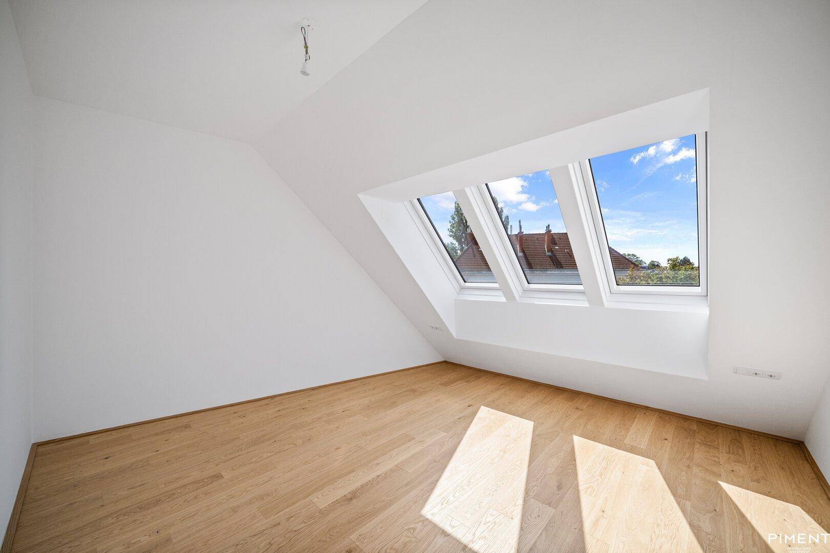 Helles Schlafzimmer im Dachgeschoss mit Holzboden und drei großen Dachfenstern.