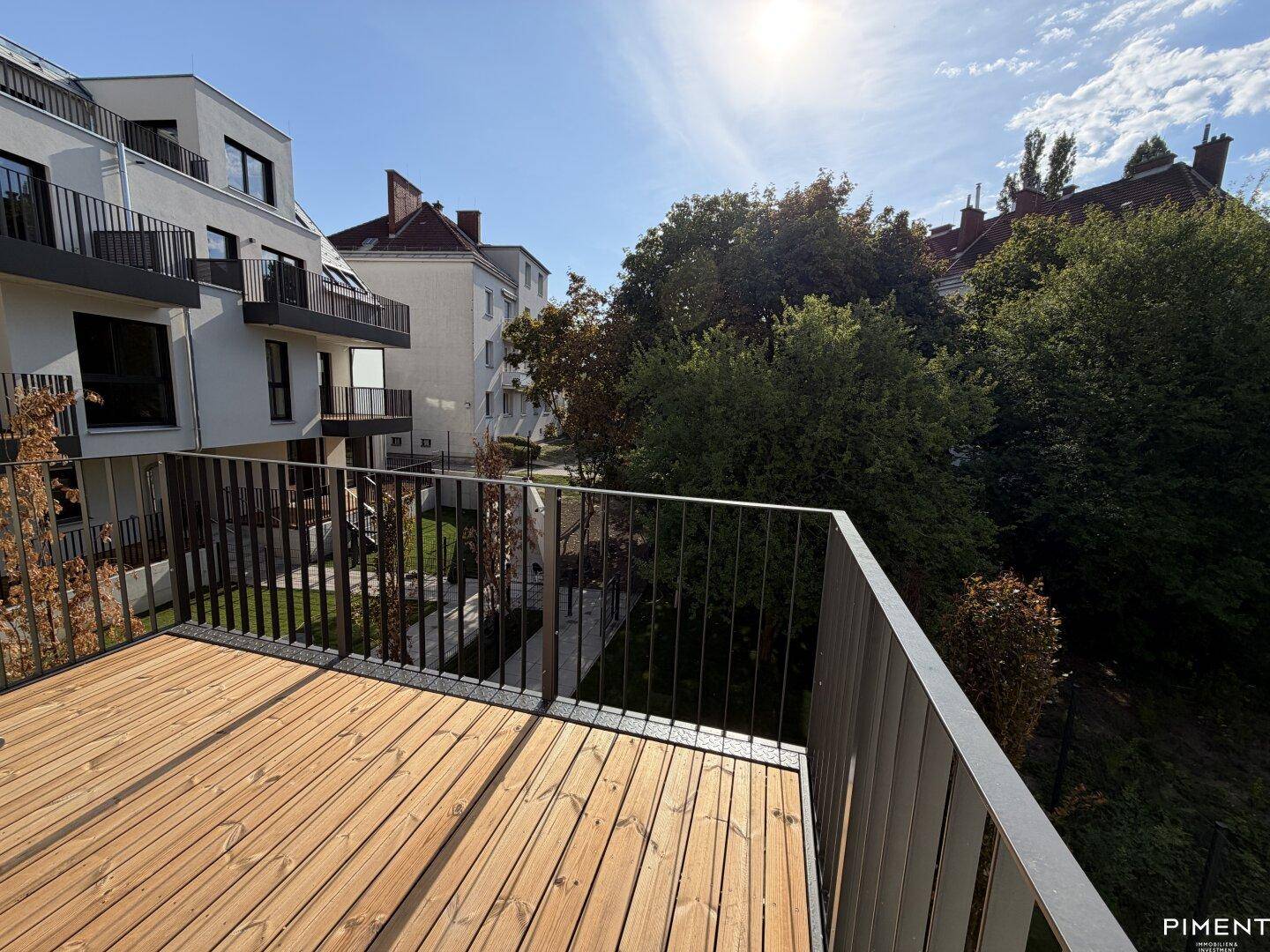 Sonniger Balkon mit Holzdielen und Blick auf die grüne Umgebung und moderne Gebäude.