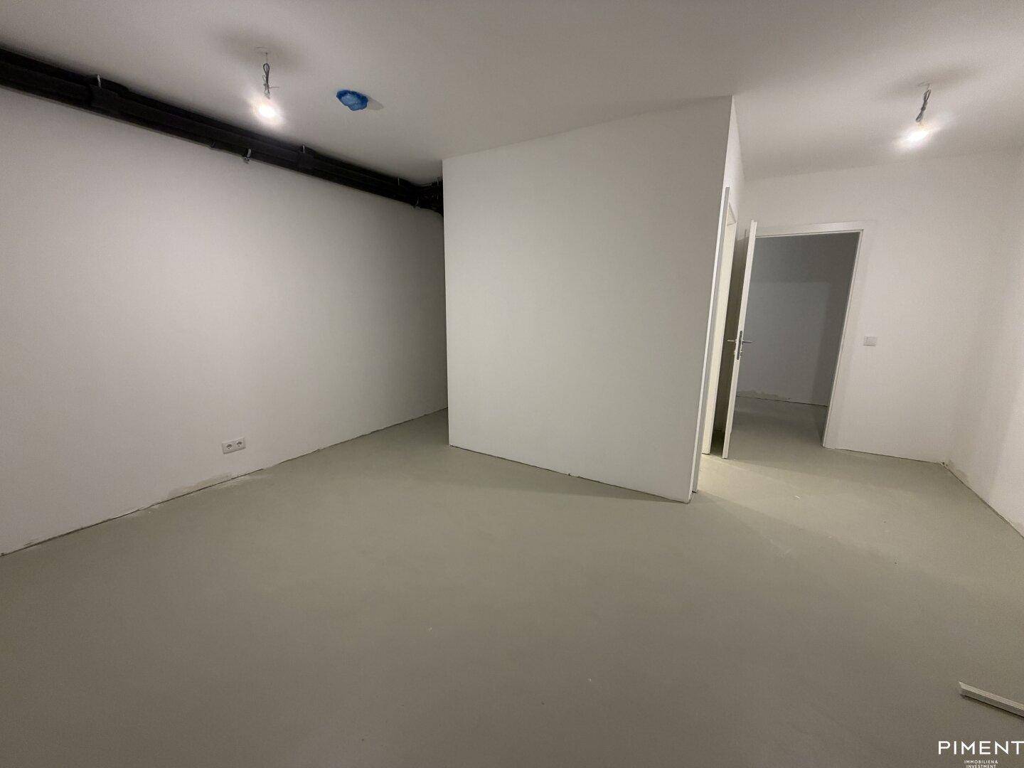 Leerer Raum mit Betonboden und sichtbaren Leitungen an der Decke, ideal als Abstellraum.