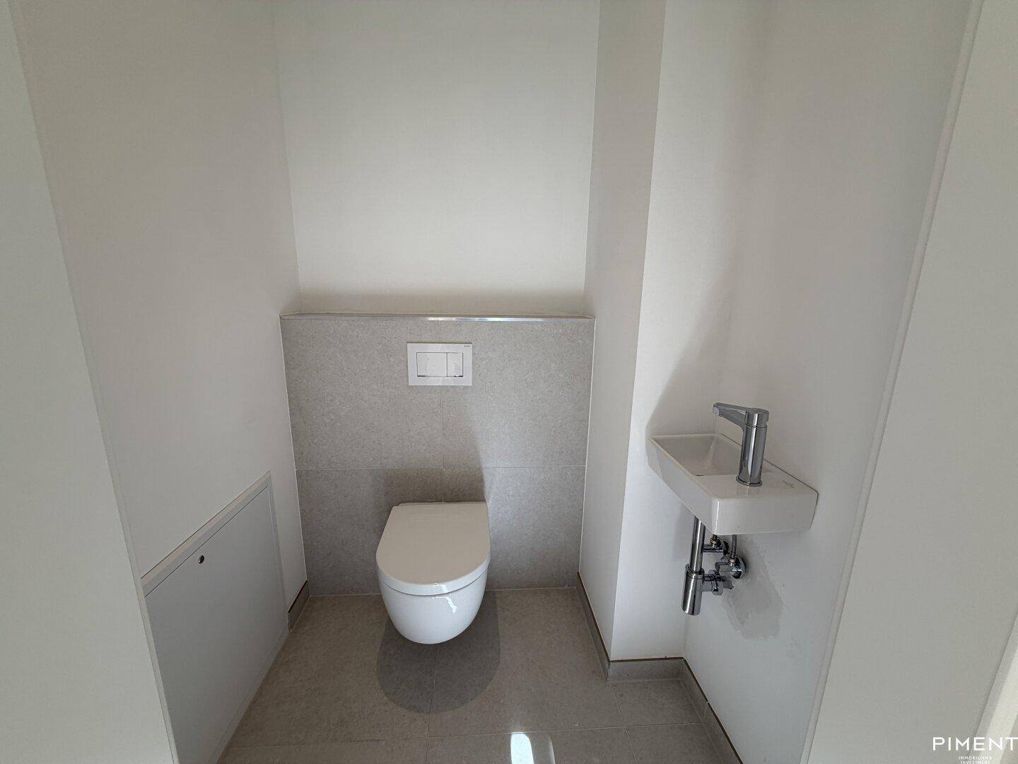 Kleines Gäste-WC mit Wand-WC und kompaktem Eckwaschbecken, modern gefliest.
