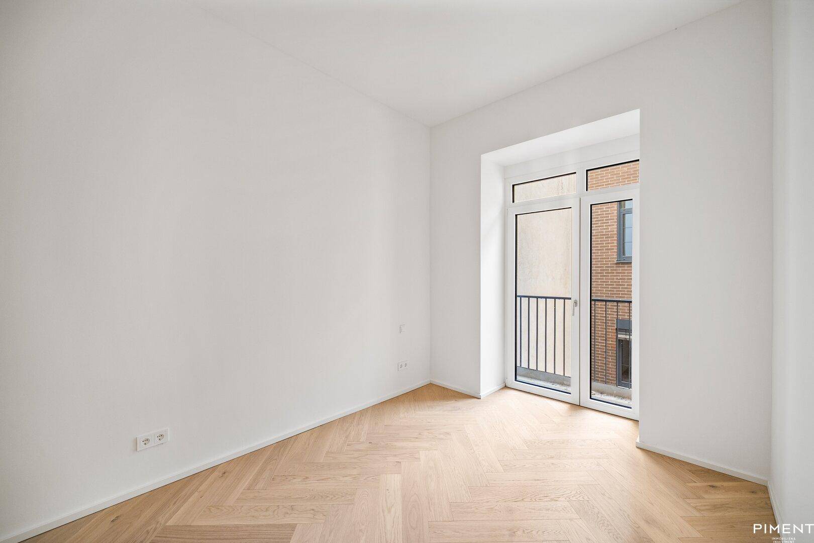 Helles Zimmer mit Fischgrätparkett und Zugang zu einem französischen Balkon.
