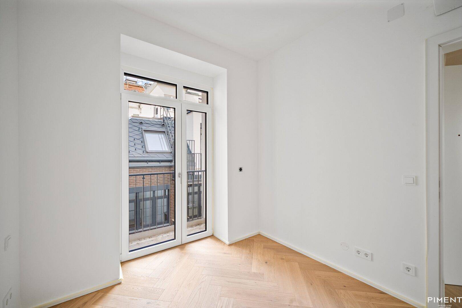Renoviertes Zimmer mit Fischgrätparkett und Zugang zu einem französischen Balkon.