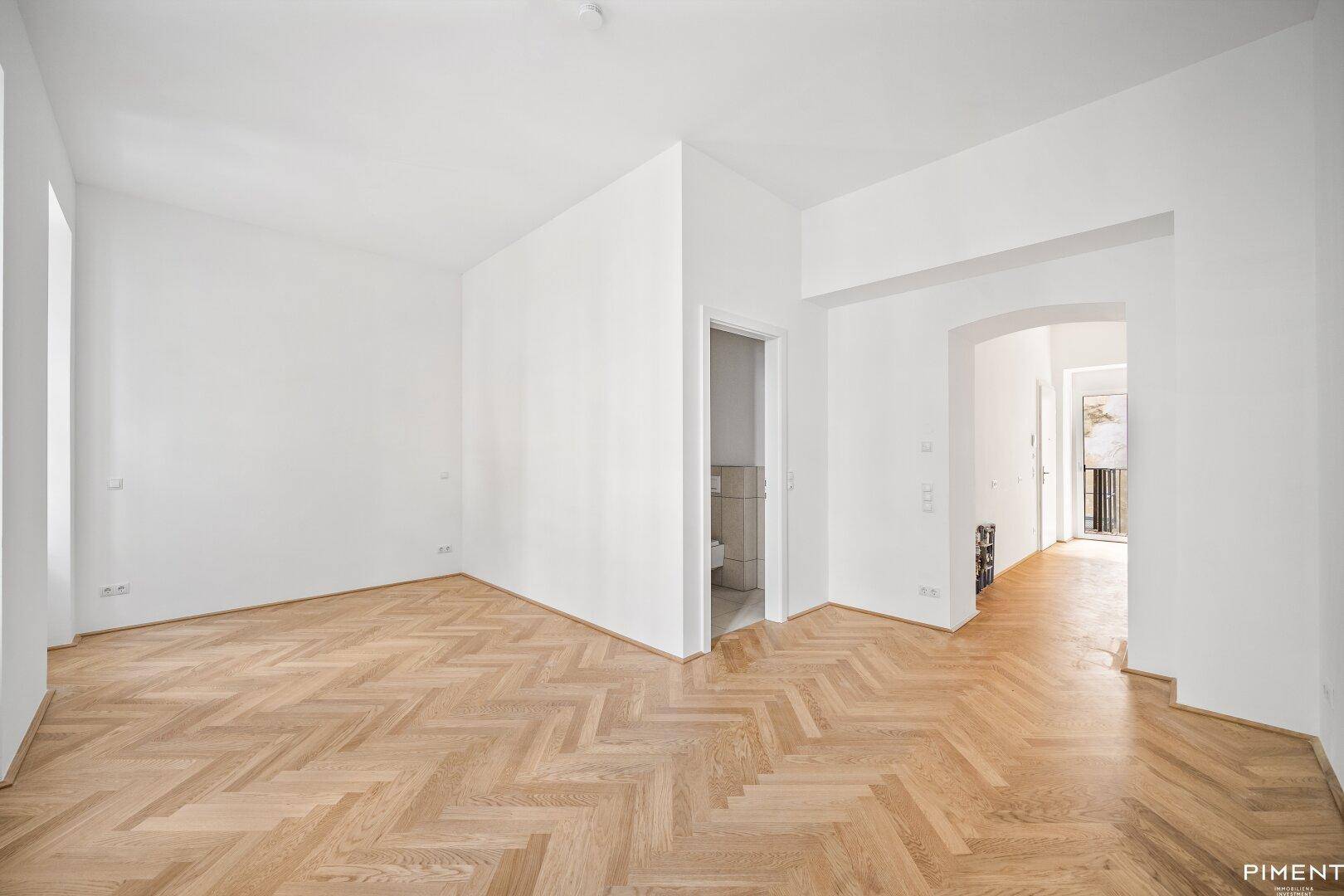 Geräumiges Zimmer mit Fischgrätparkett und Zugang zu weiteren Räumen.
