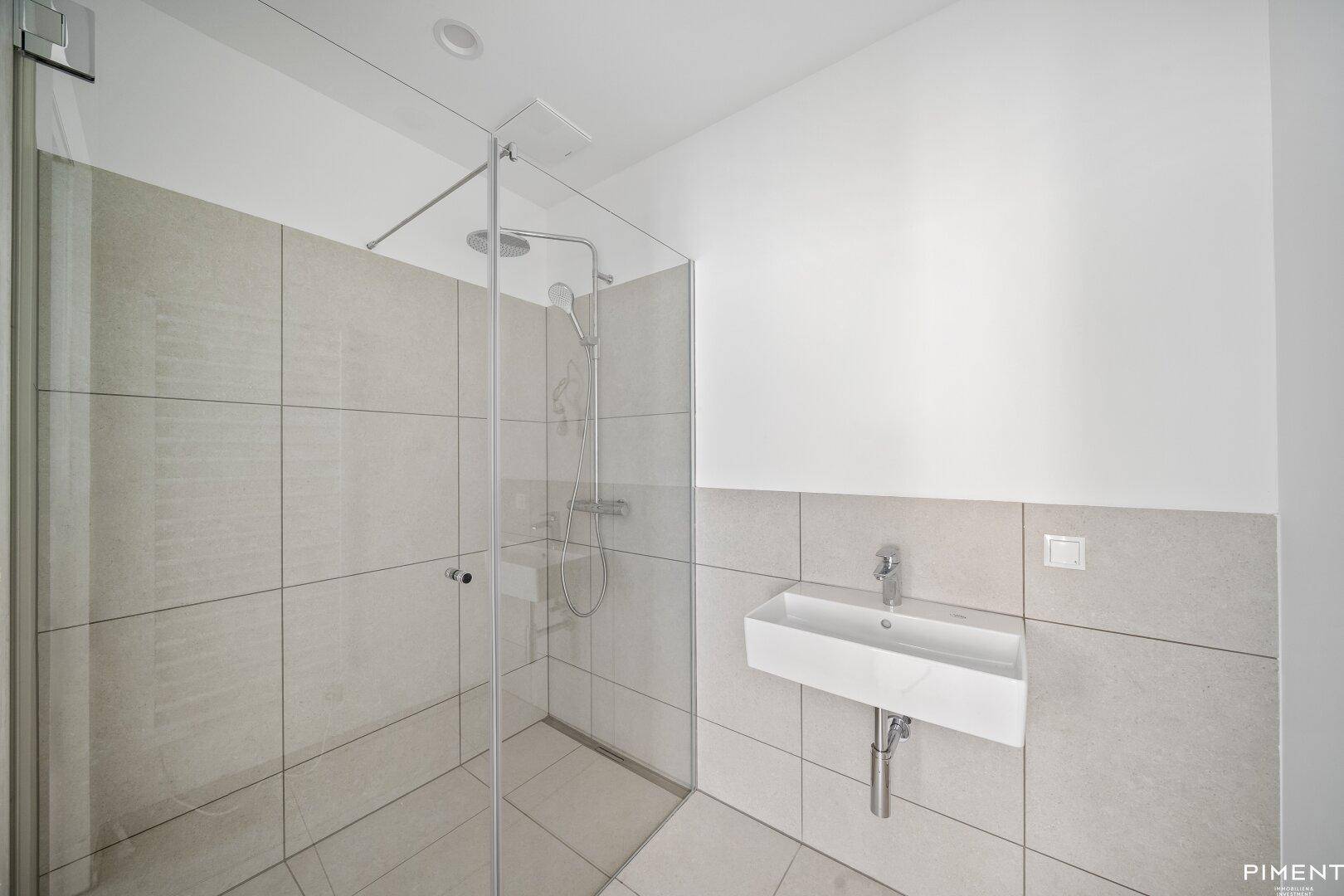 Modernes Badezimmer mit begehbarer Dusche, hellgrauen Fliesen und einem schwebenden Waschbecken.