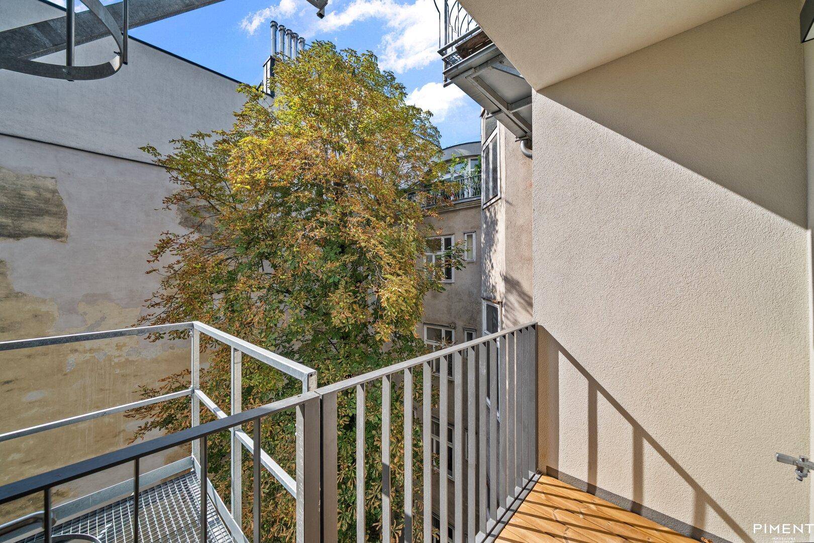 Kleiner Balkon mit Holzboden und Metallgeländer, bietet einen grünen Blick auf den Innenhof.