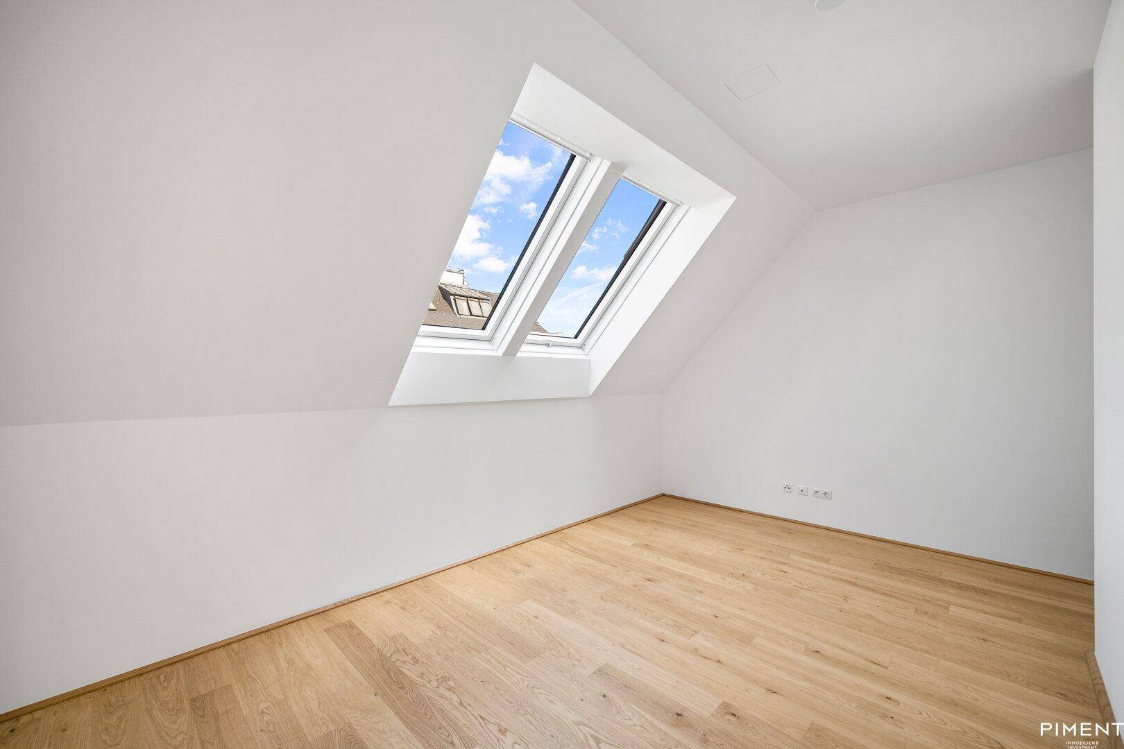 Lichtdurchflutetes Schlafzimmer mit Holzboden und schrägen Wänden unter Dachfenstern.
