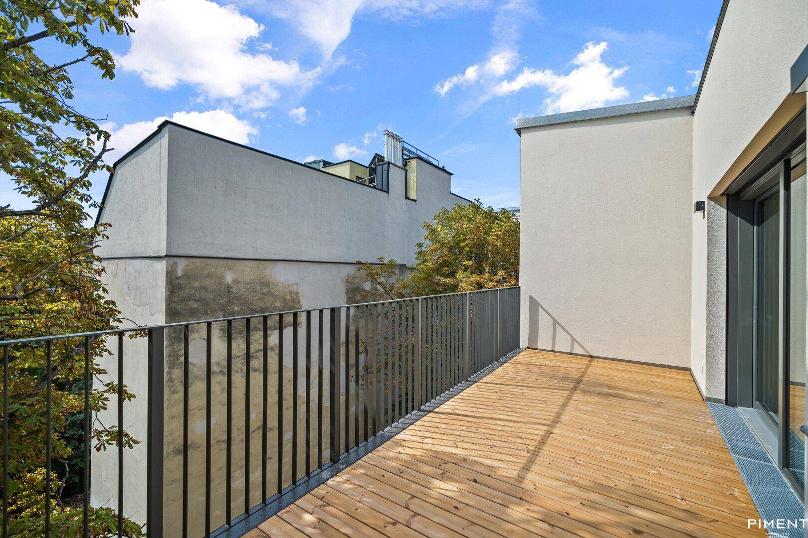 Moderne Holzterrasse mit Metallgeländer und Blick auf umliegende Gebäude und Bäume.