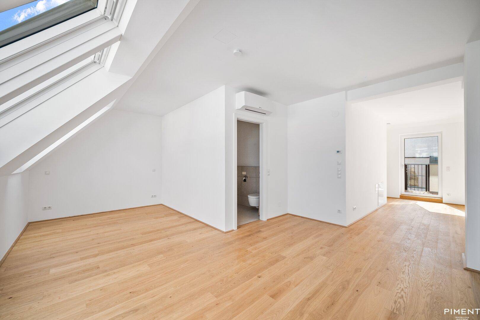 Geräumiger Dachgeschossraum mit Holzboden, Zugang zu einem WC und einem kleinen Balkon.