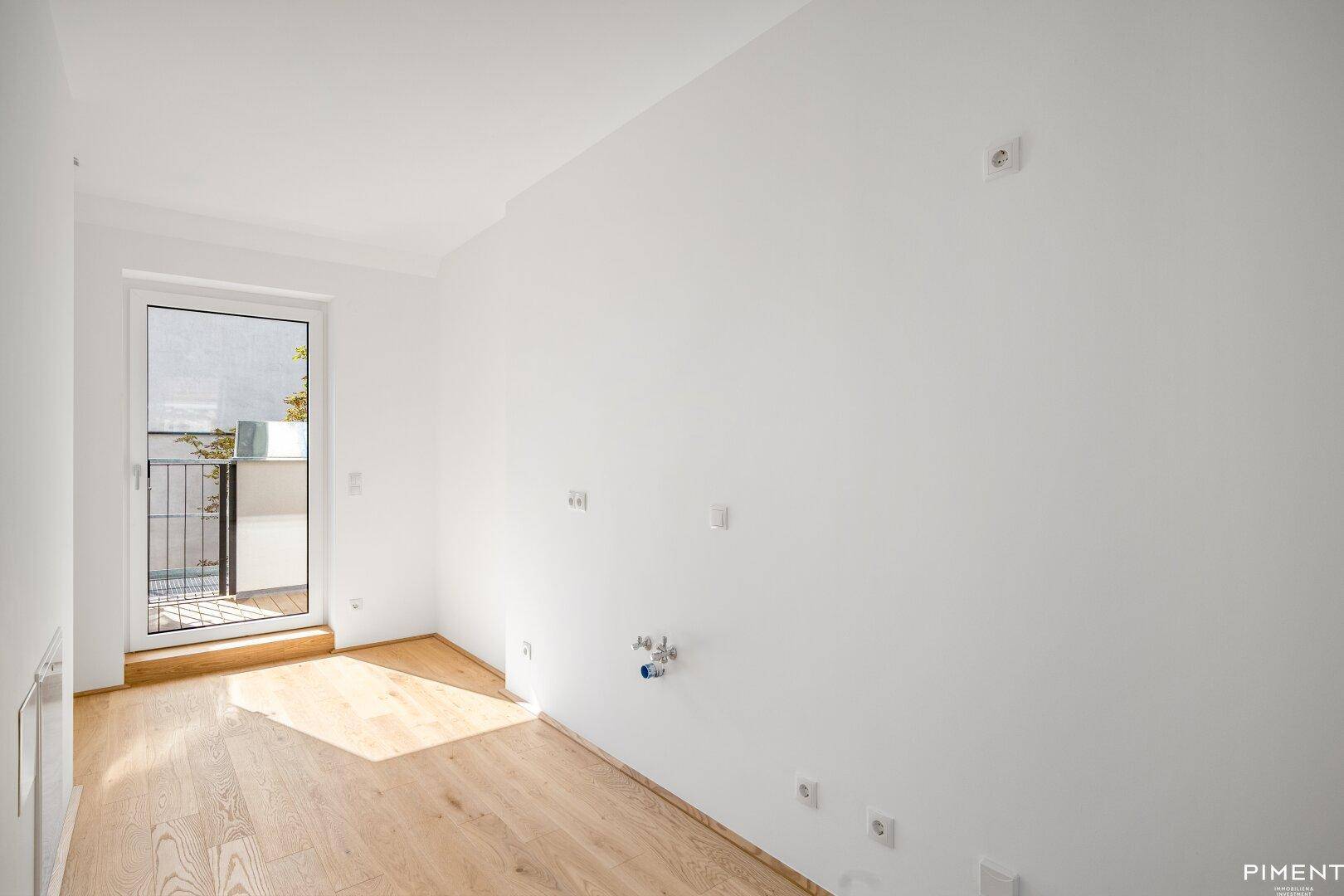 Leerer Raum mit Holzboden, Anschlussmöglichkeiten für eine Küche und Zugang zu einem Balkon.