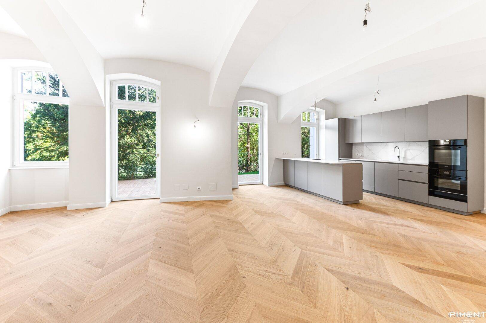 Offener Wohn- und Essbereich mit moderner Küche, Fischgrätparkett und Zugang zur Terrasse.
