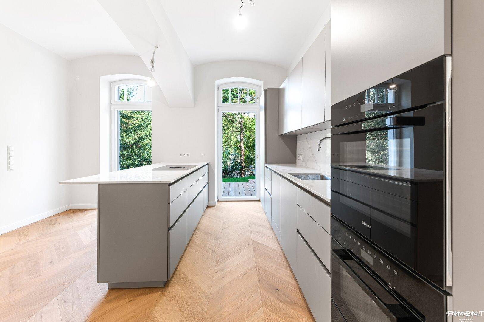 Elegante, moderne Küche mit grauen Schränken, Kochinsel und integrierten Miele-Geräten.